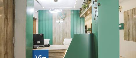 A reception desk with a 'Via' sign, a wooden desk, a computer, and a chair.