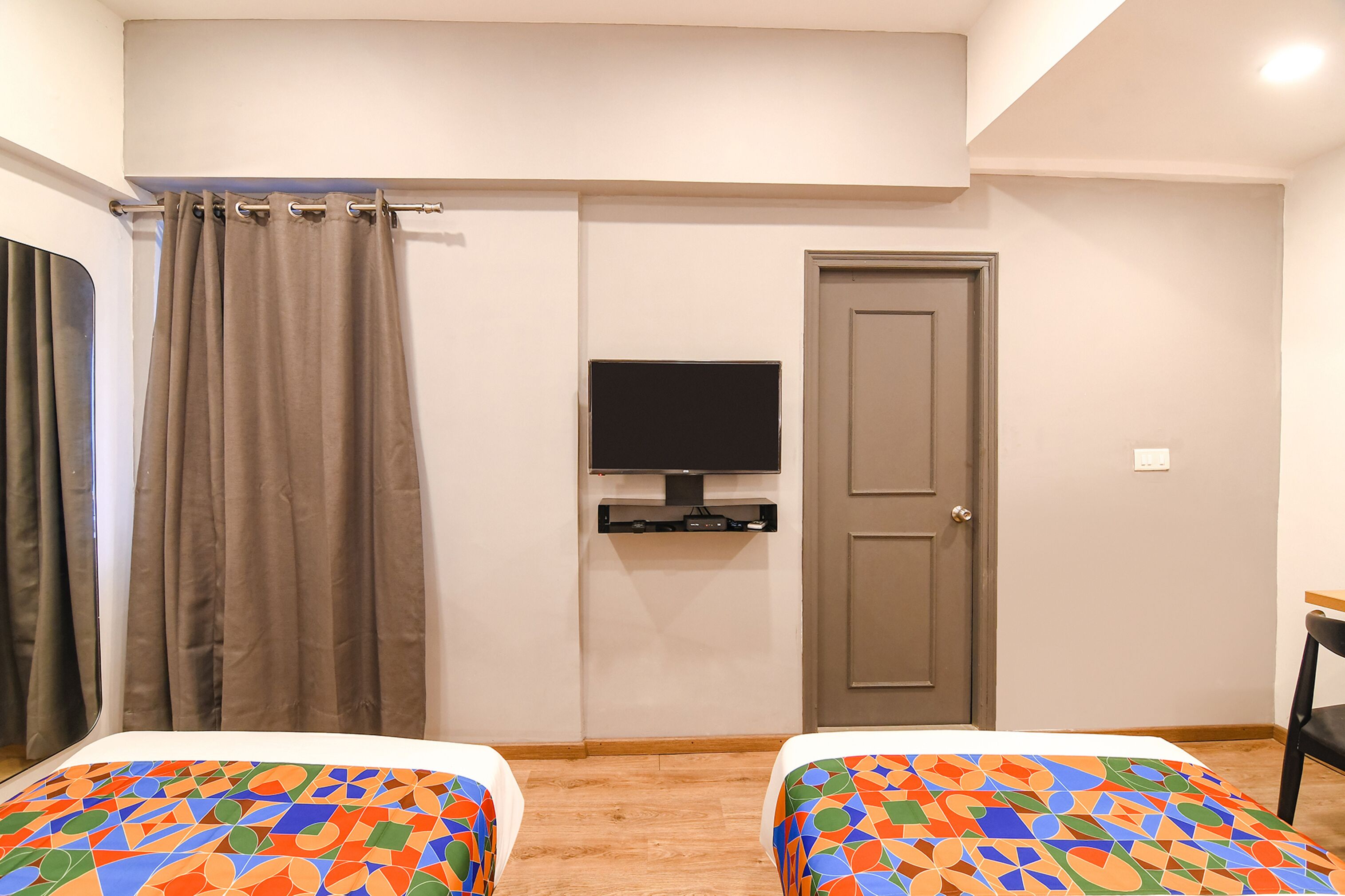A hotel room with two beds, a television mounted on the wall, a door, and a curtain.