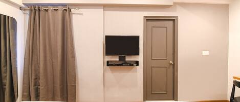 A hotel room with two beds, a television mounted on the wall, a door, and a curtain.
