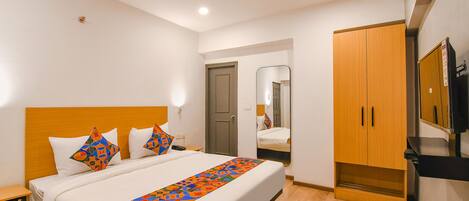 A hotel room with a bed, a wooden wardrobe, a mirror, and a television.