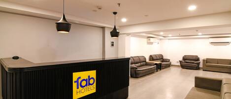 A hotel reception area with a black reception desk, multiple sofas, and ceiling lights.