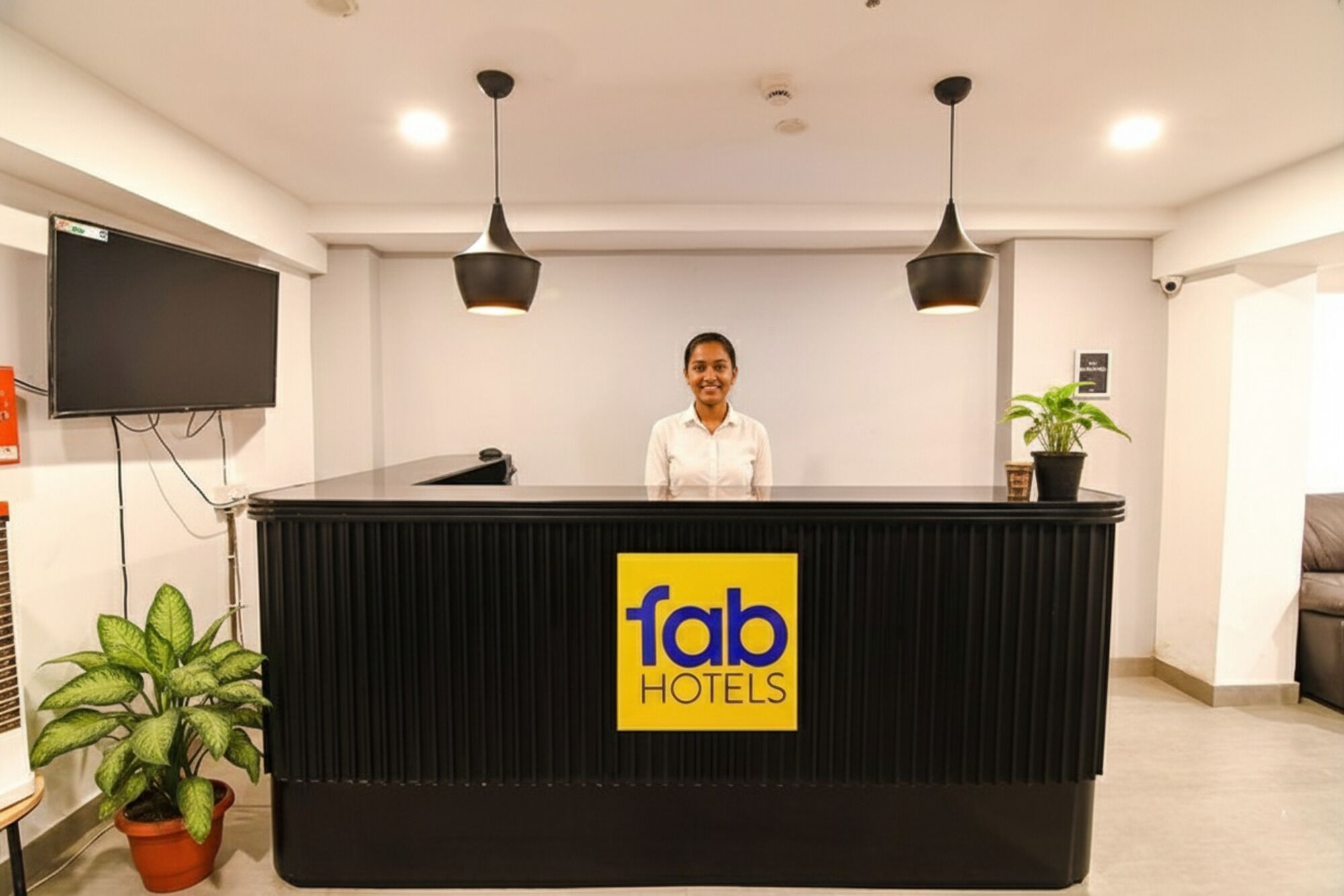 Un comptoir d’accueil avec une enseigne indiquant « fab hotels », deux lampes suspendues, un téléviseur à écran plat et une plante en pot.