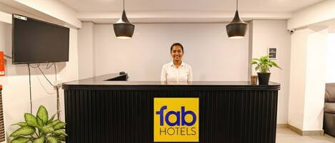Un comptoir d’accueil avec une enseigne indiquant « fab hotels », deux lampes suspendues, un téléviseur à écran plat et une plante en pot.