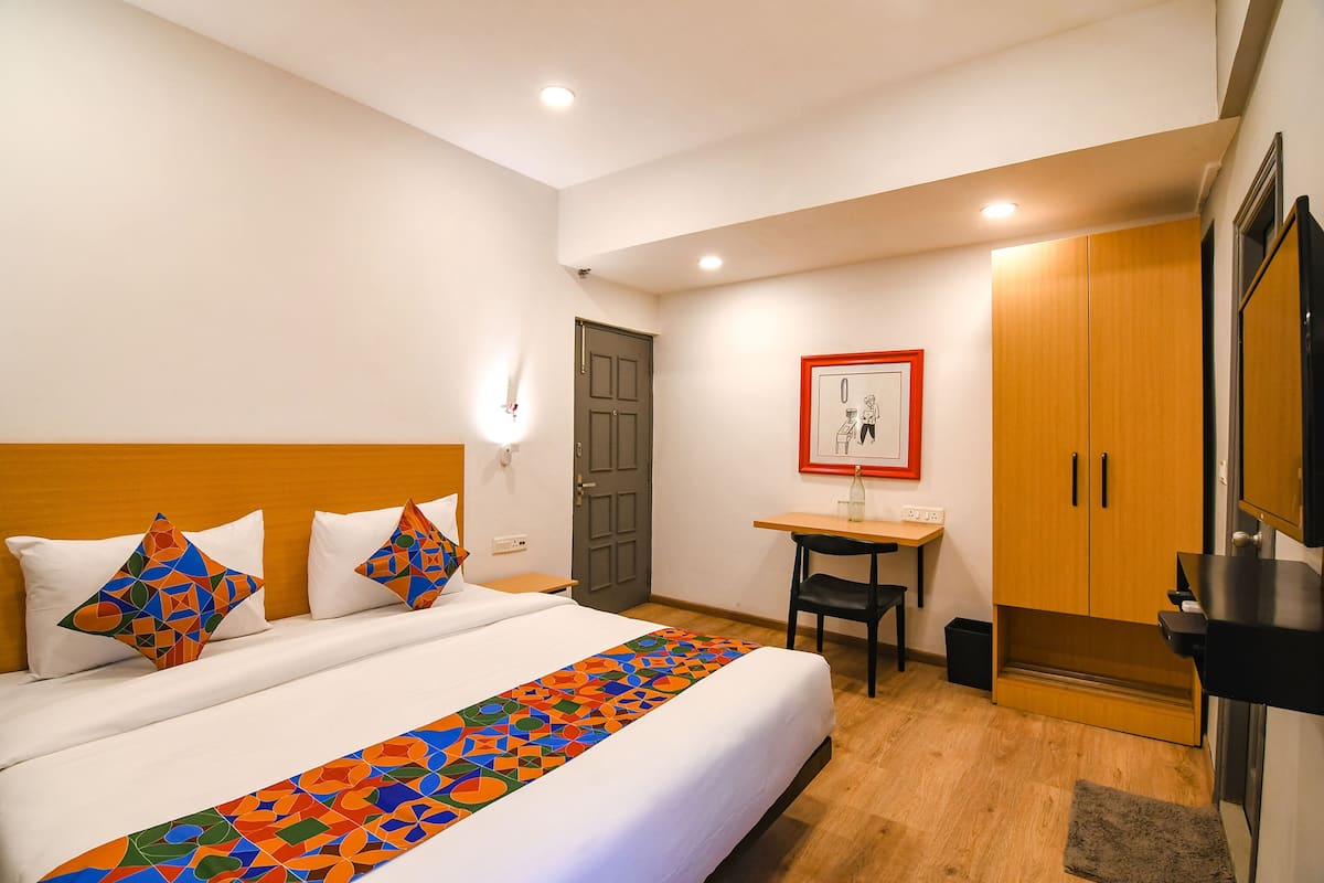 Quarto de hotel com cama, escrivaninha, cadeira, guarda-roupa e televisão.