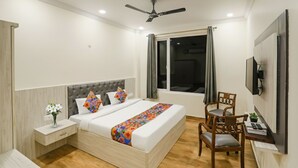 A bedroom with a bed, bedside tables, a desk, a chair, a TV, and a ceiling fan. - FabHotel Trijal Inn (Lucknow)