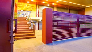 A modern building entrance with a staircase leading to a second floor, a closed shutter door, and a security gate. - FabHotel Trijal Inn (Lucknow)