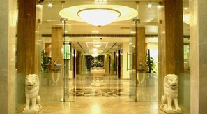 A hotel lobby with a grand chandelier, marble flooring, and two lion statues at the entrance. - Fabhotel Prime Hampshire Plaza (Hyderabad)