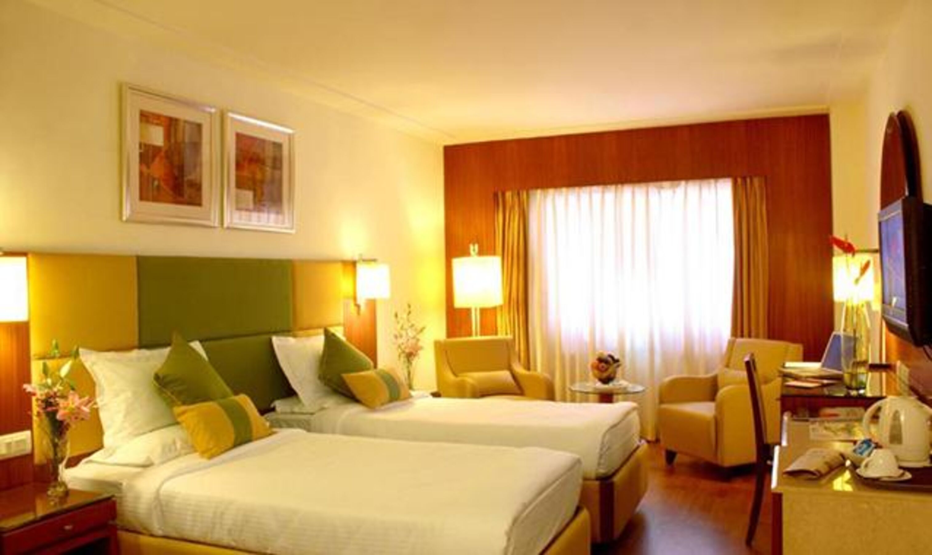 A hotel room with two beds, a desk, a chair, a television, and a window with curtains.