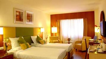 A hotel room with two beds, a desk, a chair, a television, and a window with curtains.