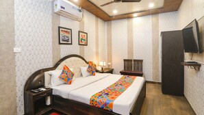 Habitación de hotel con cama, mesita de noche, lámpara, silla, televisor y aire acondicionado.