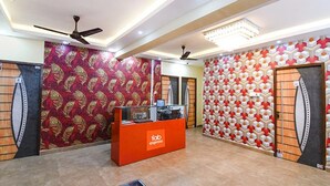 Un vestíbulo con paredes decoradas, un mostrador de recepción, ventiladores de techo y piso de baldosas.