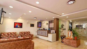 A hotel reception area with a reception desk, two sofas, and a decorative plant. - Fabhotel Red Coral (Haridwar)