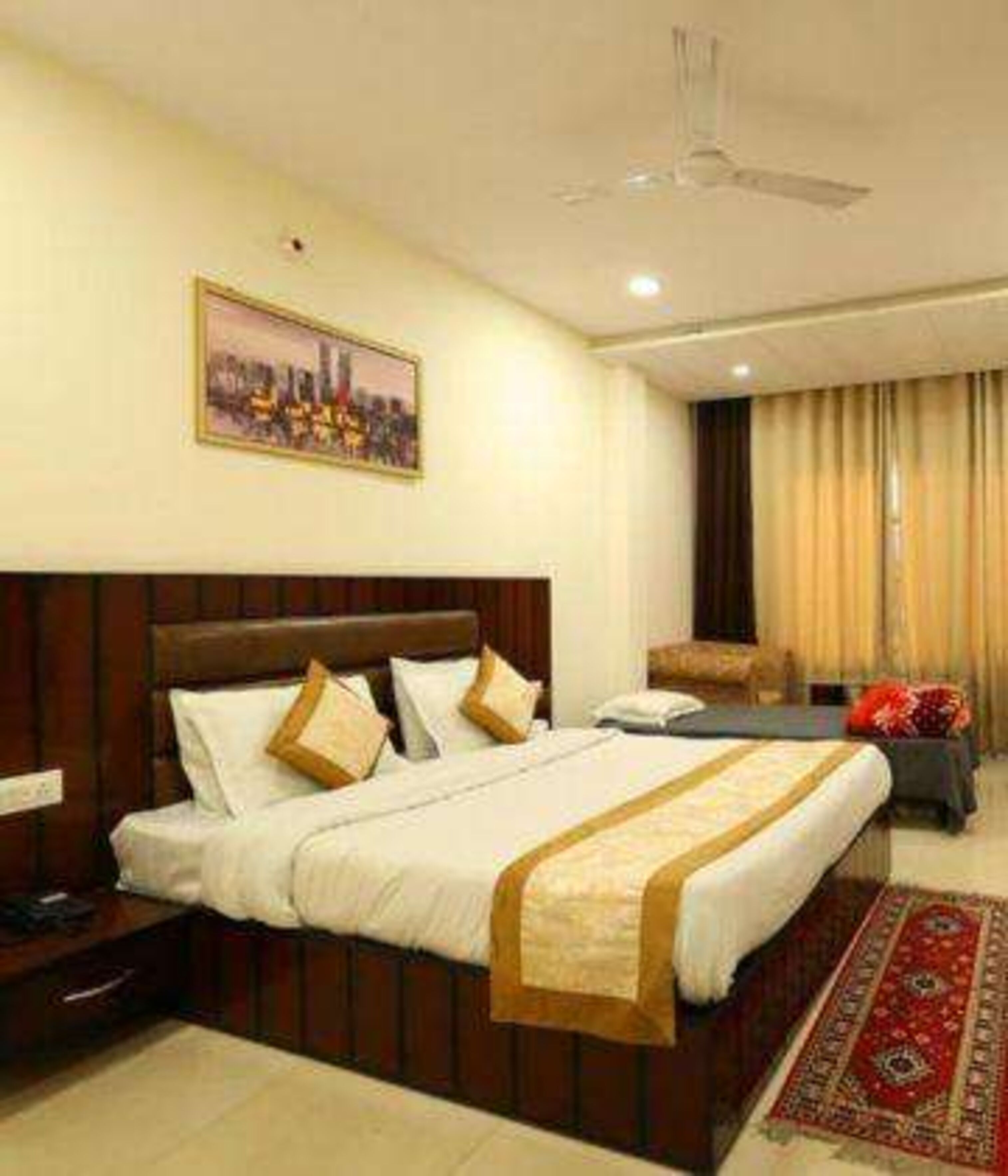 A hotel room with a large bed, a desk, a chair, a nightstand, and a window with curtains.