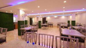 A spacious dining area with multiple tables and chairs, a green accent wall, and recessed ceiling lighting. - Fabhotel Red Coral (Haridwar)