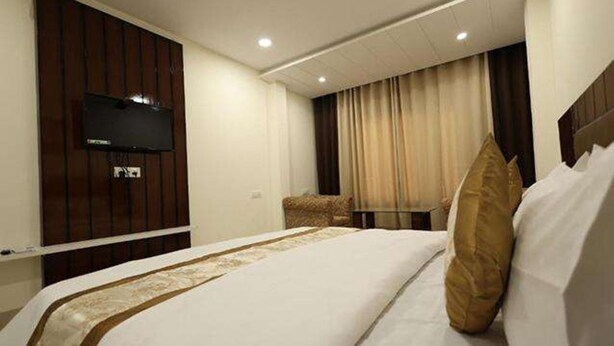 A hotel room with a large bed, a flat-screen TV mounted on the wall, a small table, and a chair. - Fabhotel Red Coral (Haridwar)