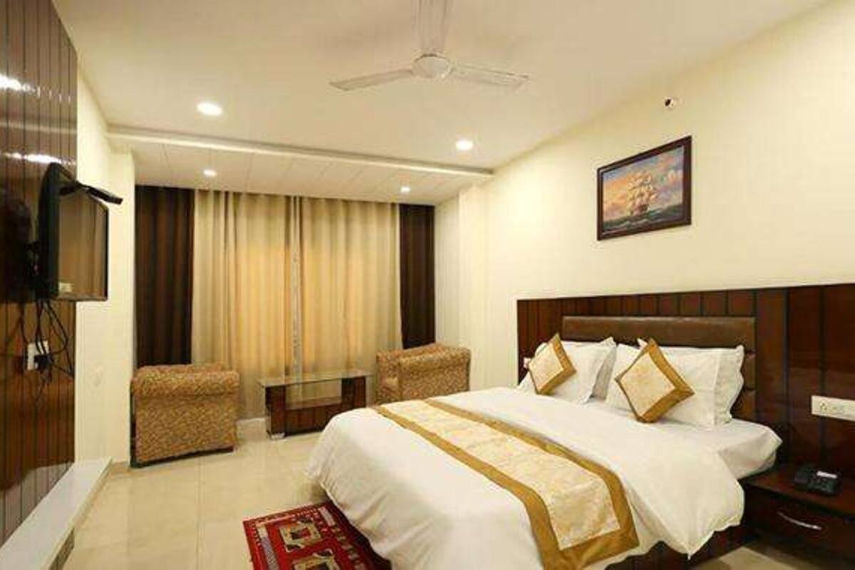 A hotel room with a large bed, two armchairs, a TV, and a painting on the wall.
