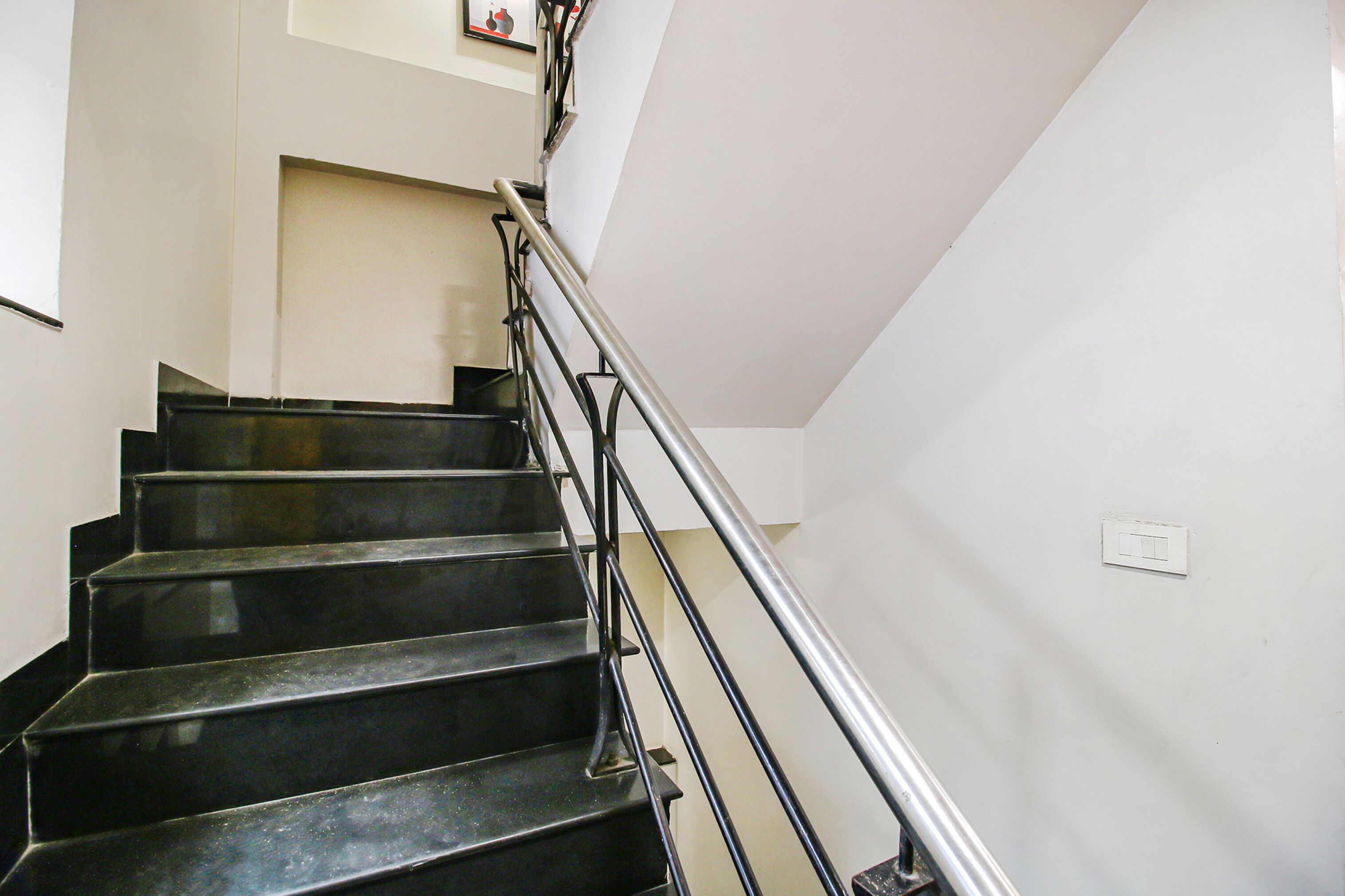 Eine Treppe mit schwarzen Stufen und einem Metallgeländer, die zu einem Landeplatz mit Lichtschalter führt.