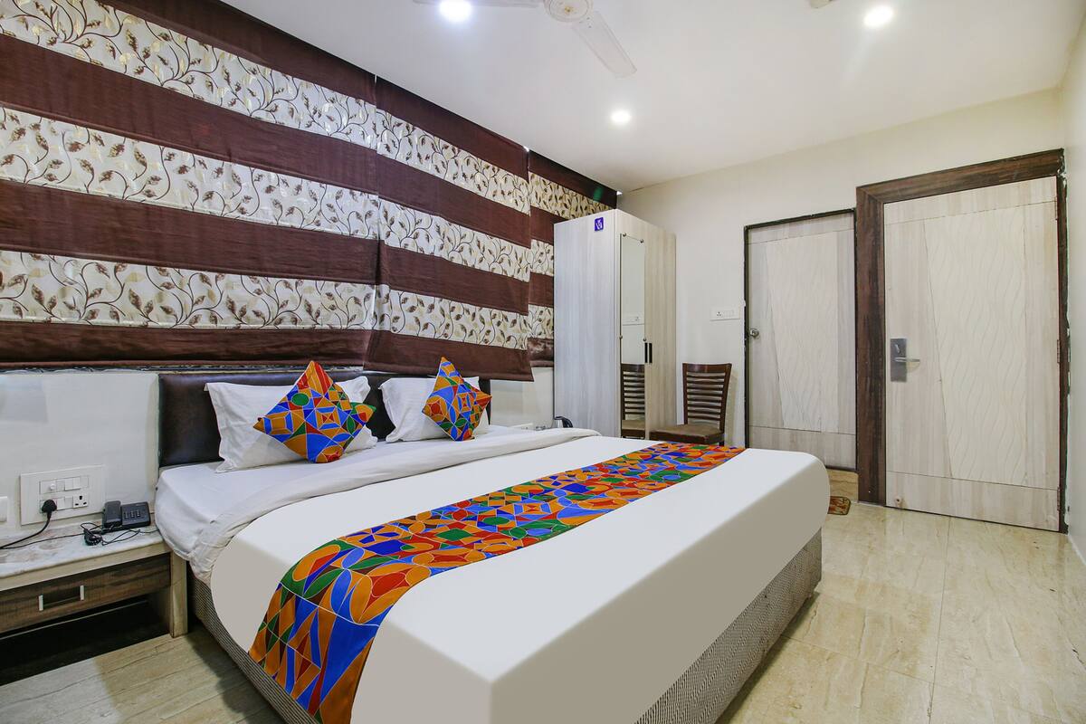 Quarto de hotel bem arrumado com uma cama grande, mesa de cabeceira, guarda-roupa e uma porta.