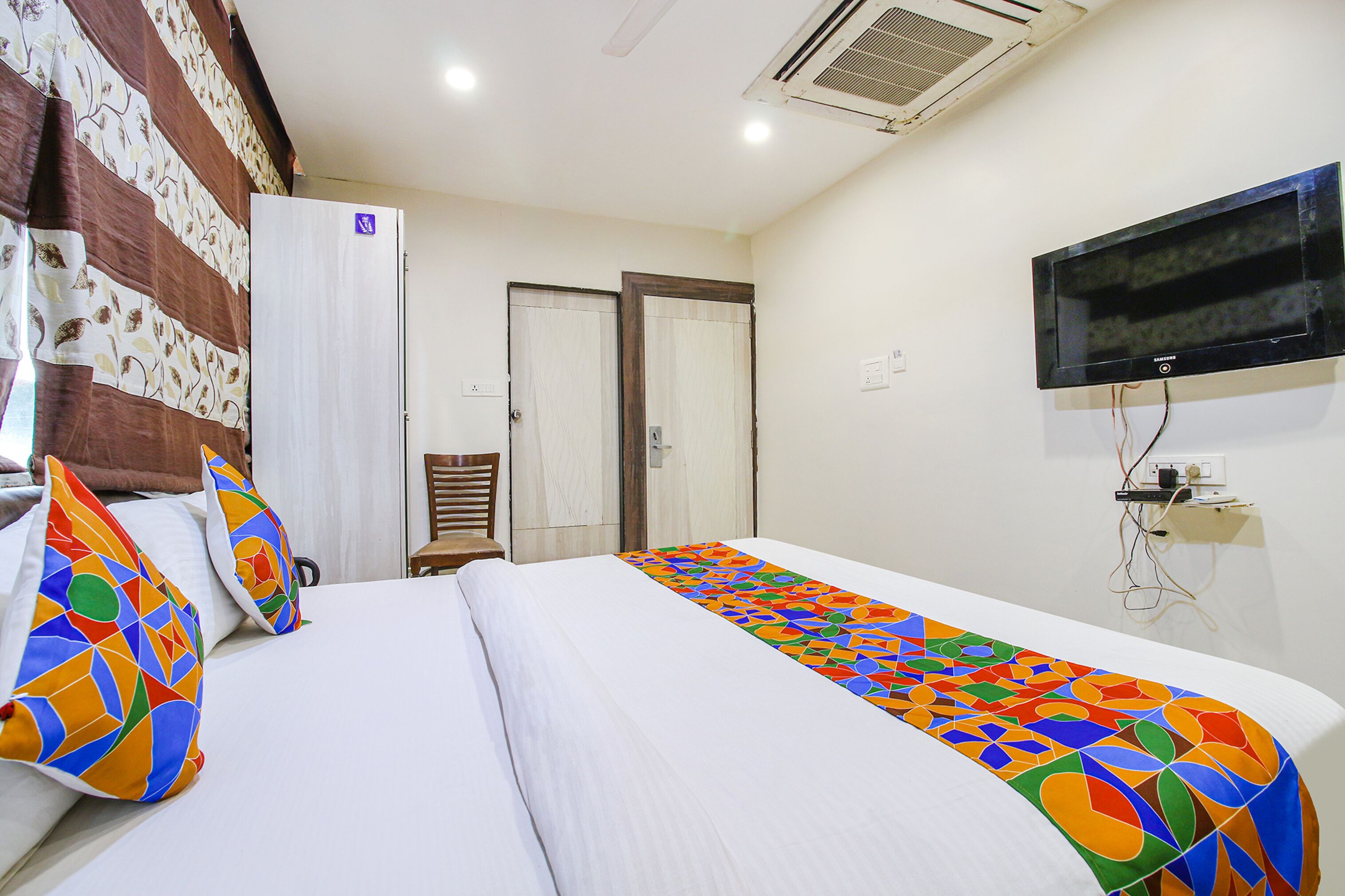 A hotel room with a bed, a TV, a wardrobe, and a chair.
