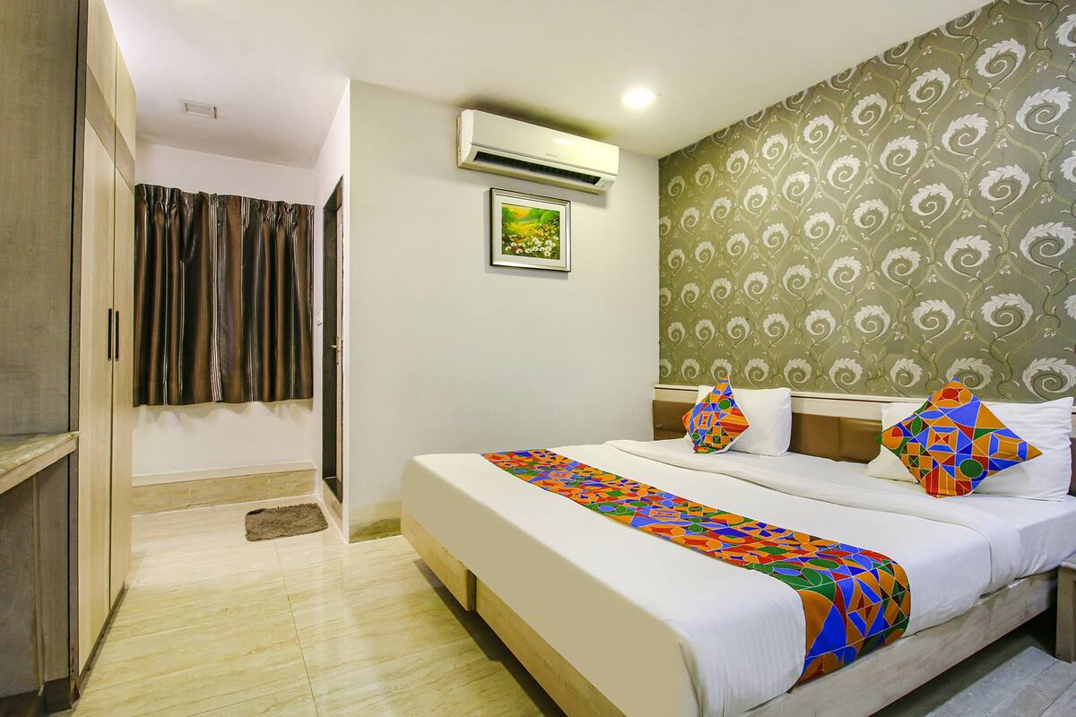 Quarto de hotel com uma cama, mesa de cabeceira, aparelho de ar condicionado, uma porta e papel de parede estampado.