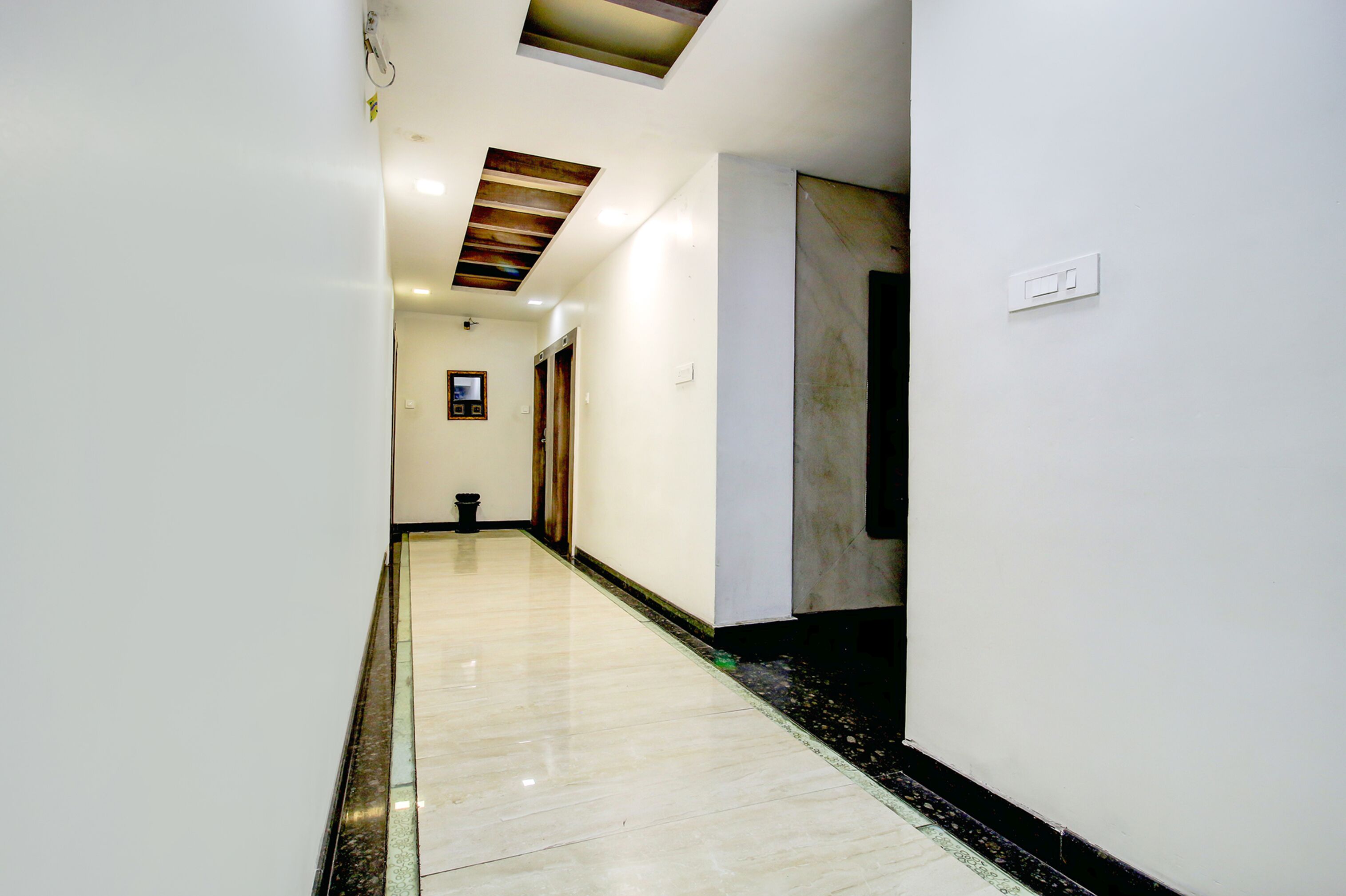Un corridoio con pavimento lucido, una lampada a soffitto e una porta con stipite scuro.