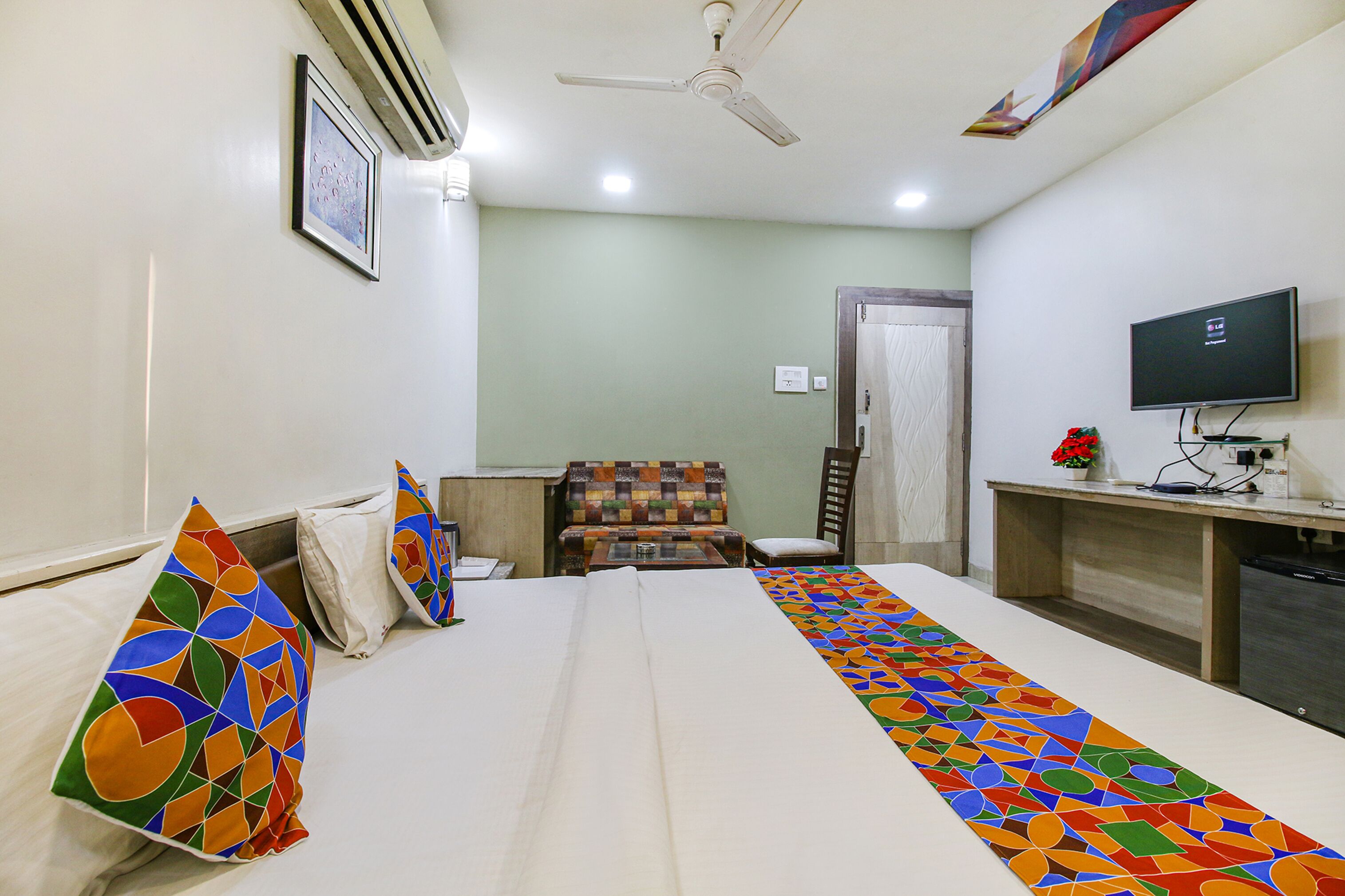 A hotel room with a bed, a desk, a chair, a television, and a ceiling fan.