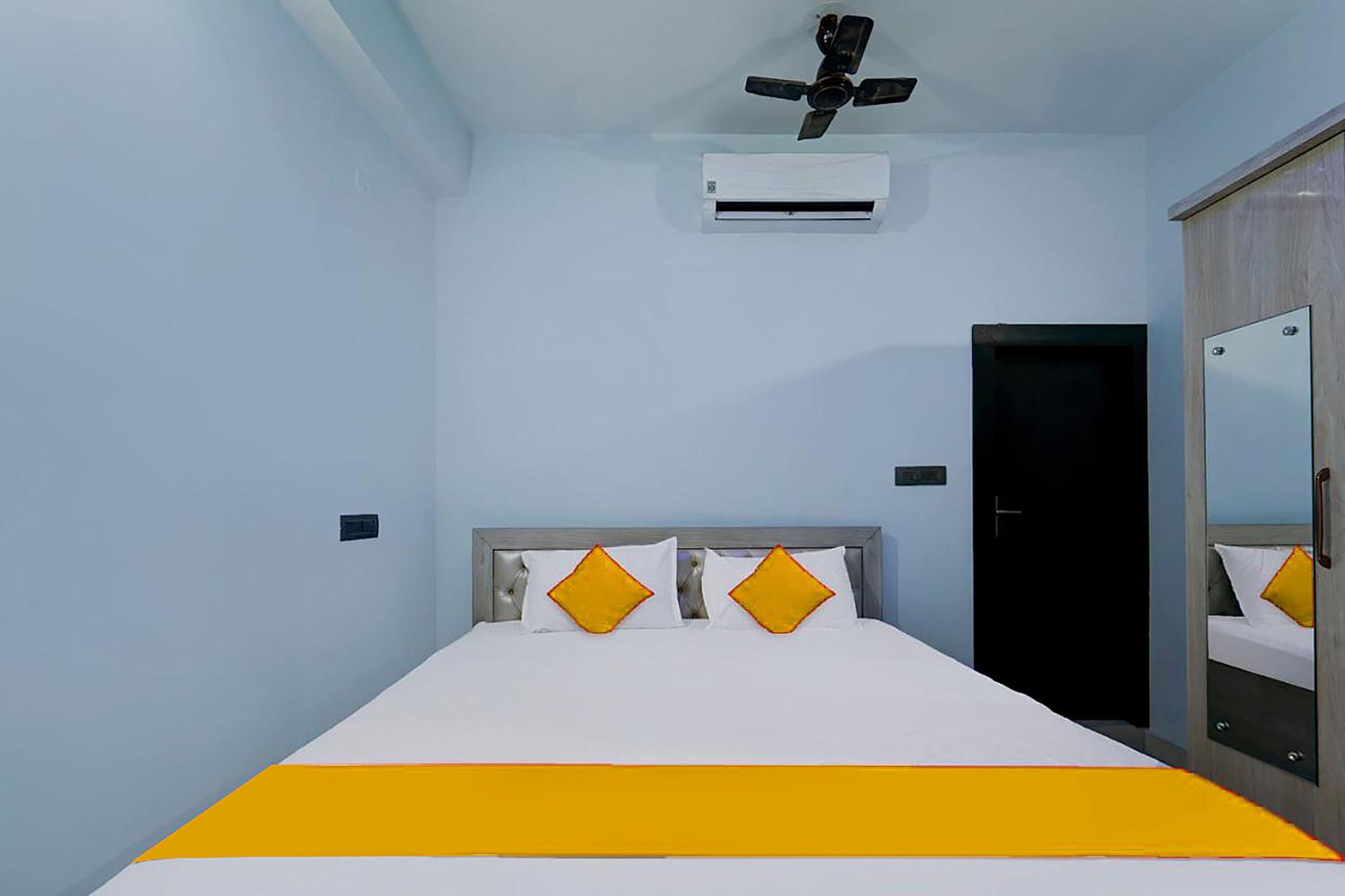 A hotel room with a bed, a ceiling fan, an air conditioning unit, a wardrobe, and a door.