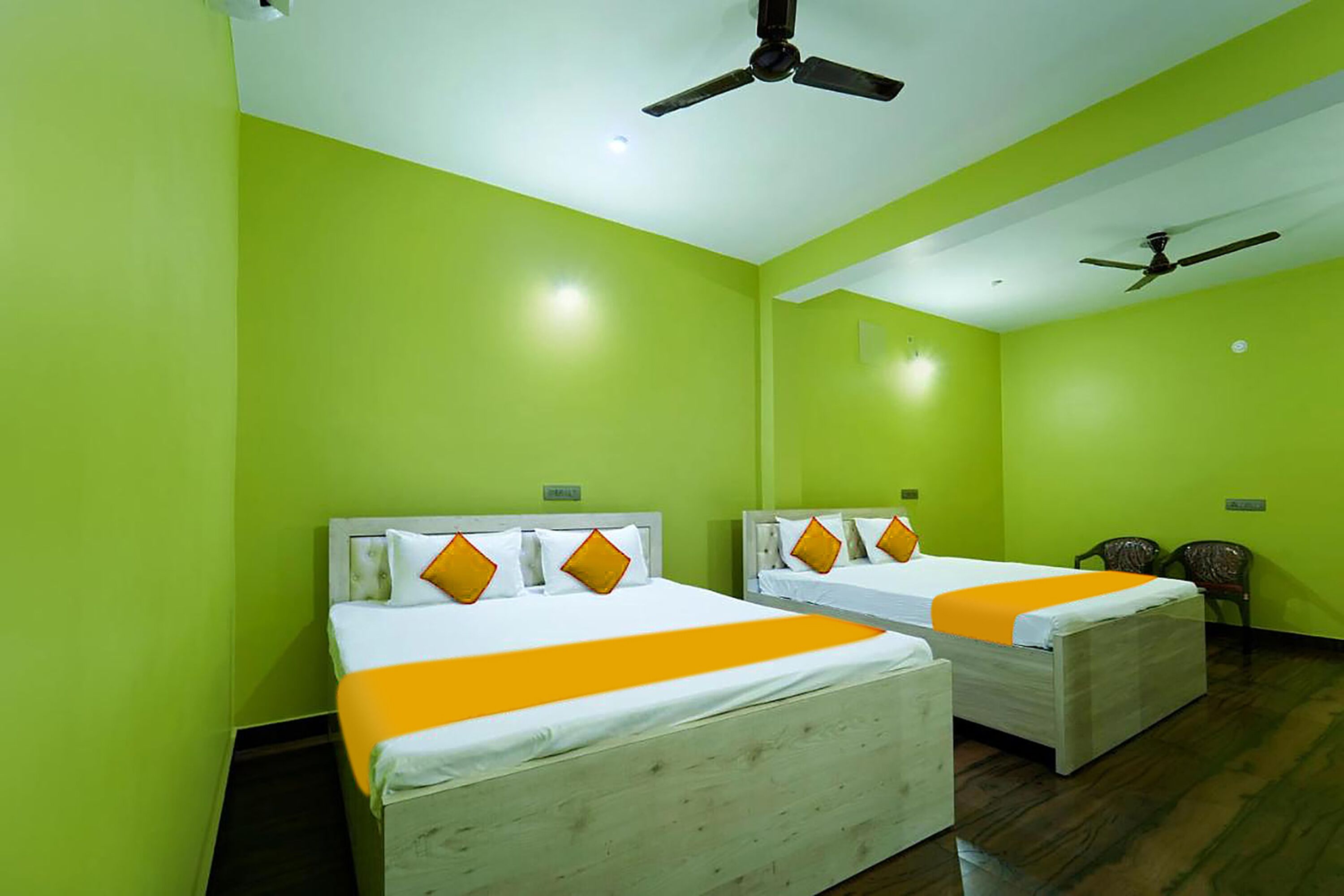 A hotel room with two beds, each with white bedding and orange accents. There are ceiling fans and a small chair in the room.