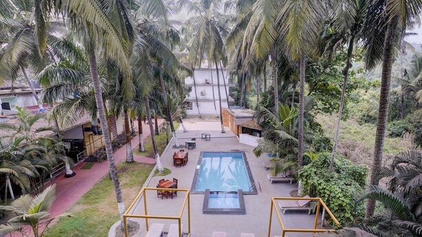 A pool area with lounge chairs and a table, surrounded by palm trees and a building in the background. - Oriva Shourya Residency (Pune)