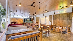 A restaurant interior with wooden tables, chairs, ceiling fans, and a brick wall. - Oriva Shourya Residency (Pune)