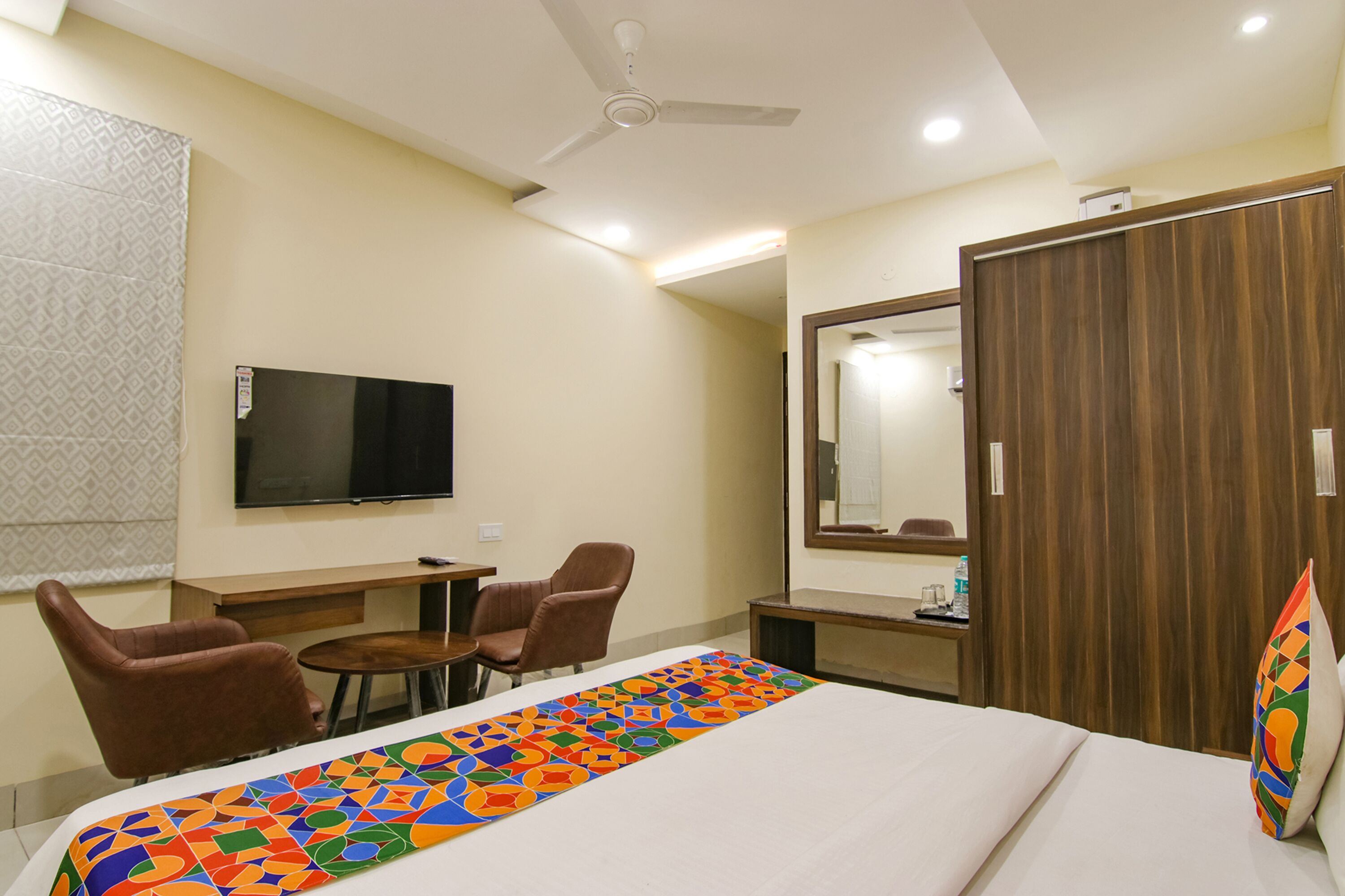 A hotel room with a bed, a TV, a desk with chairs, and a wardrobe.
