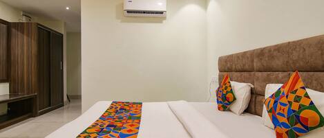 Quarto de hotel com cama, um tapete de cor vibrante com padrão geométrico, cabeceira marrom e unidade de ar condicionado.
