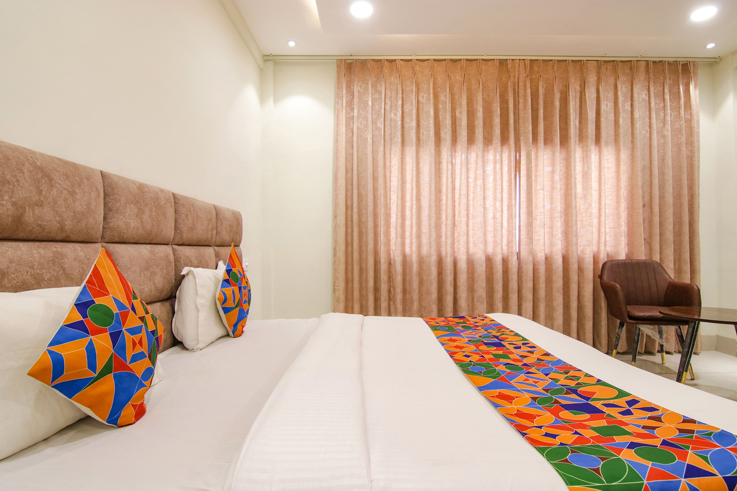 A hotel room with a large bed, a headboard, a chair, and a window with curtains.