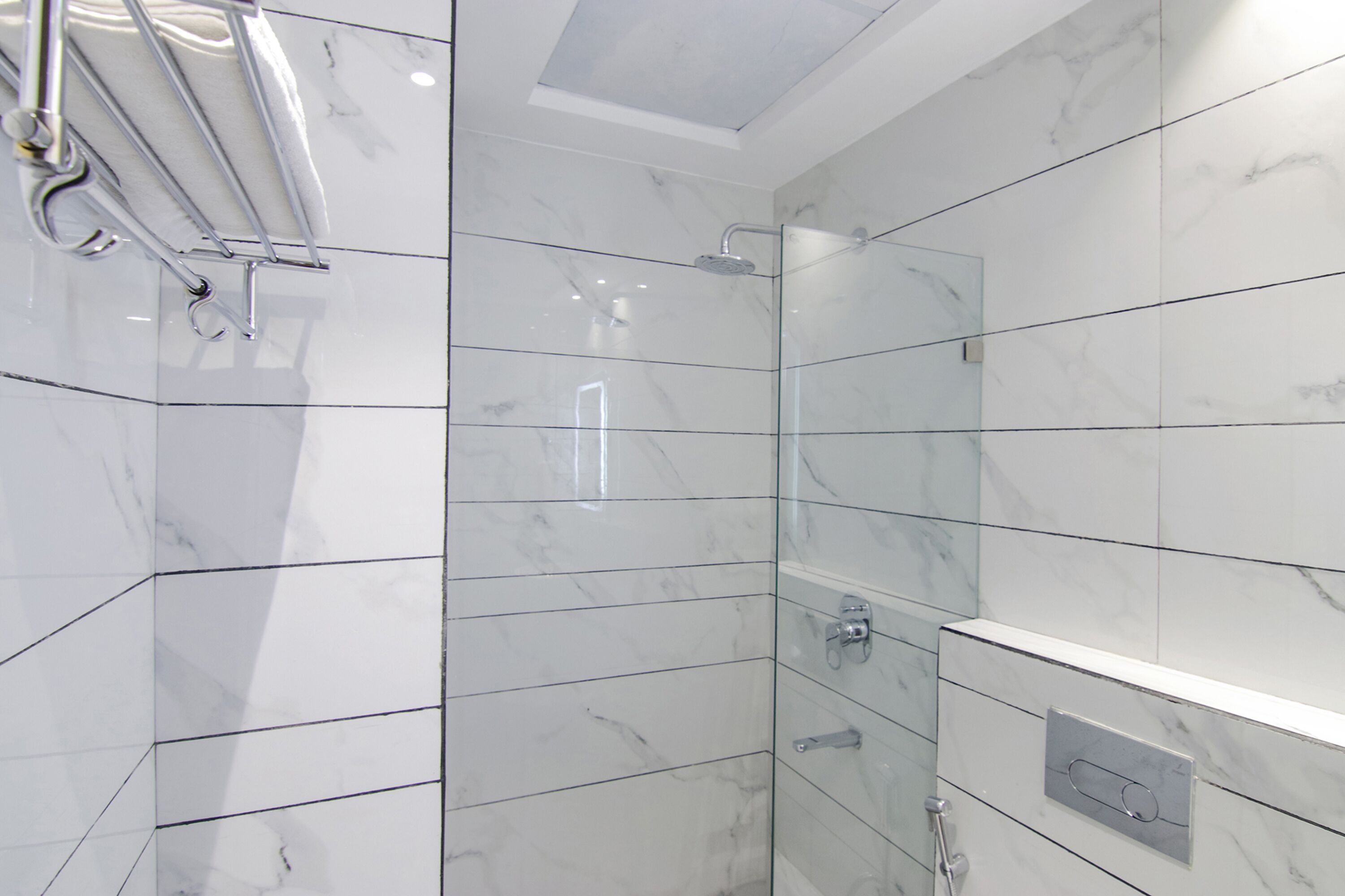 Une salle de bain moderne avec des carreaux de marbre blanc, une douche en verre et une étagère intégrée.