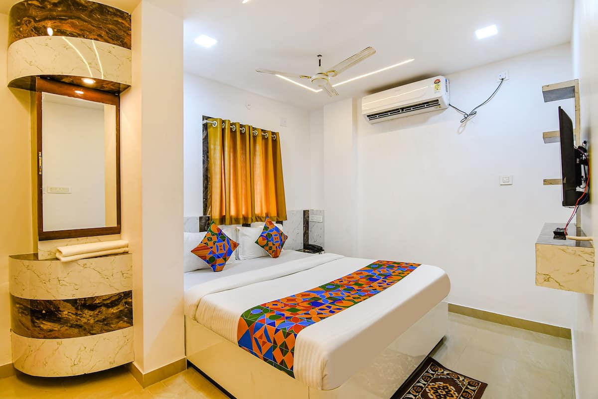 A hotel room with a bed, a bathroom, a mirror, an air conditioning unit, and a television.