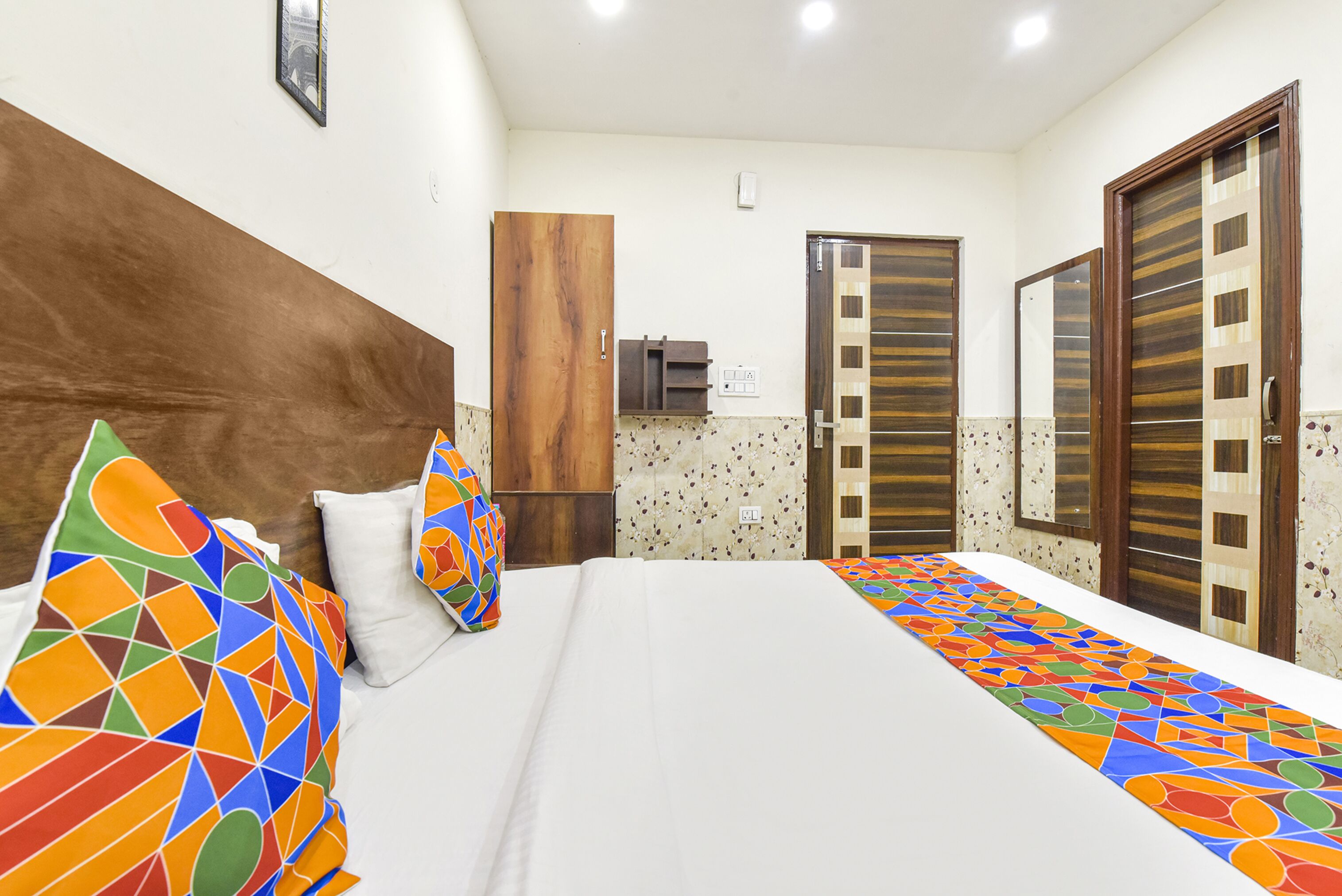 Una habitación de hotel con una cama grande, almohadas de colores, un cabecero de madera, un armario y un espejo.