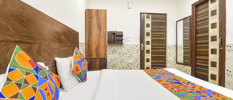 Una habitación de hotel con una cama grande, almohadas de colores, un cabecero de madera, un armario y un espejo.
