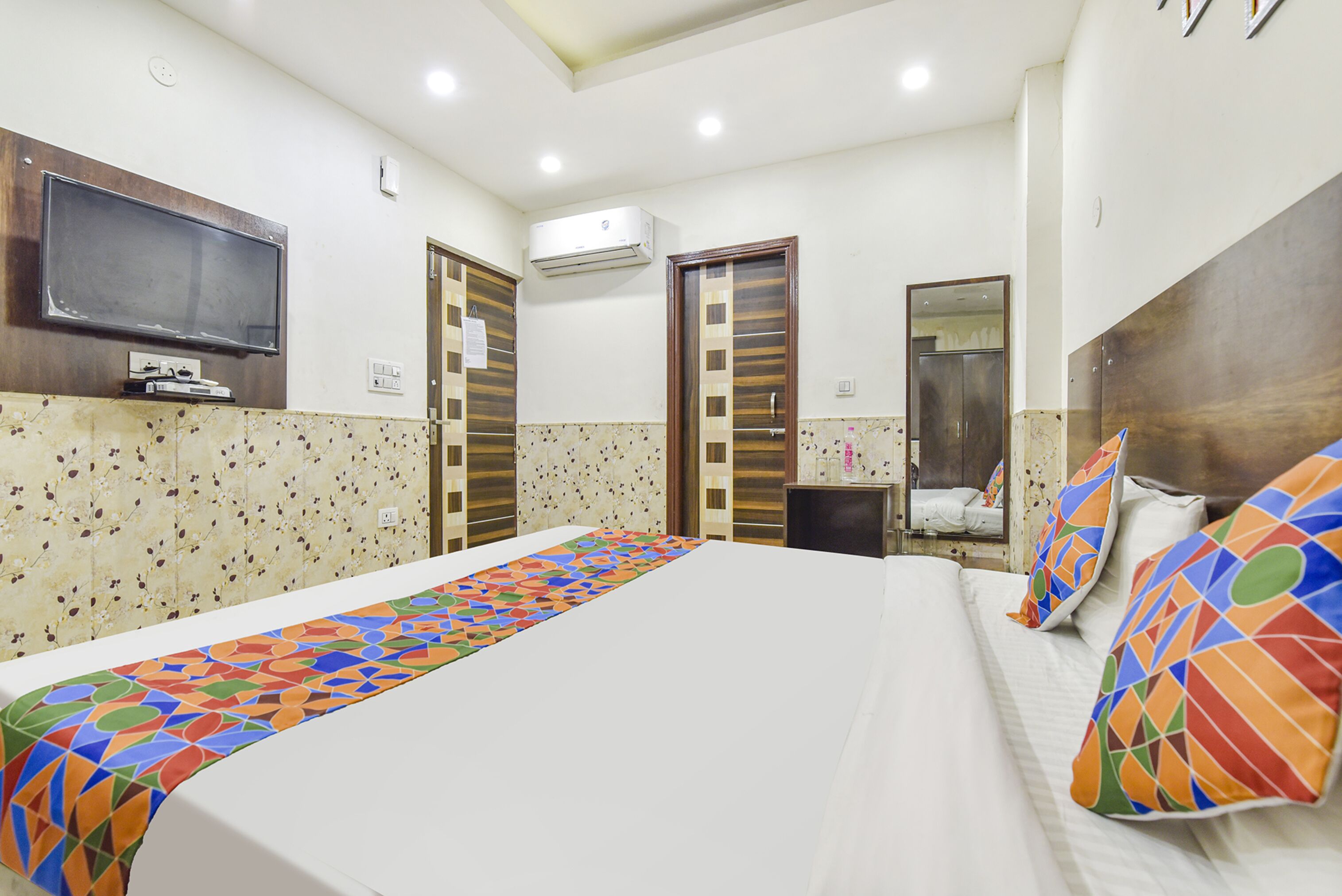 A hotel room with a large bed, a flat-screen TV mounted on the wall, an air conditioning unit, and a shower area.