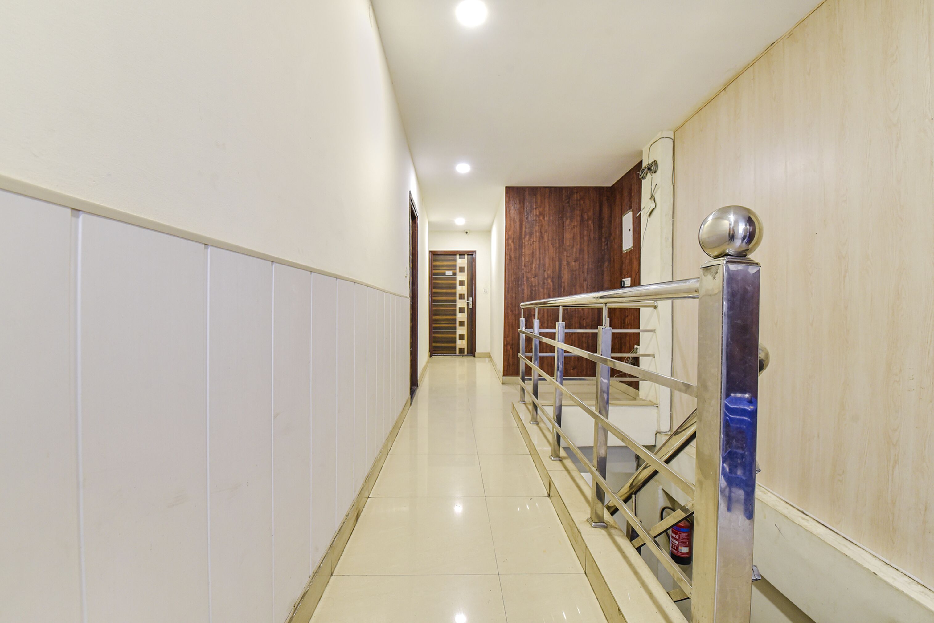 A hallway with a metal railing, a wooden door, and a white wall.