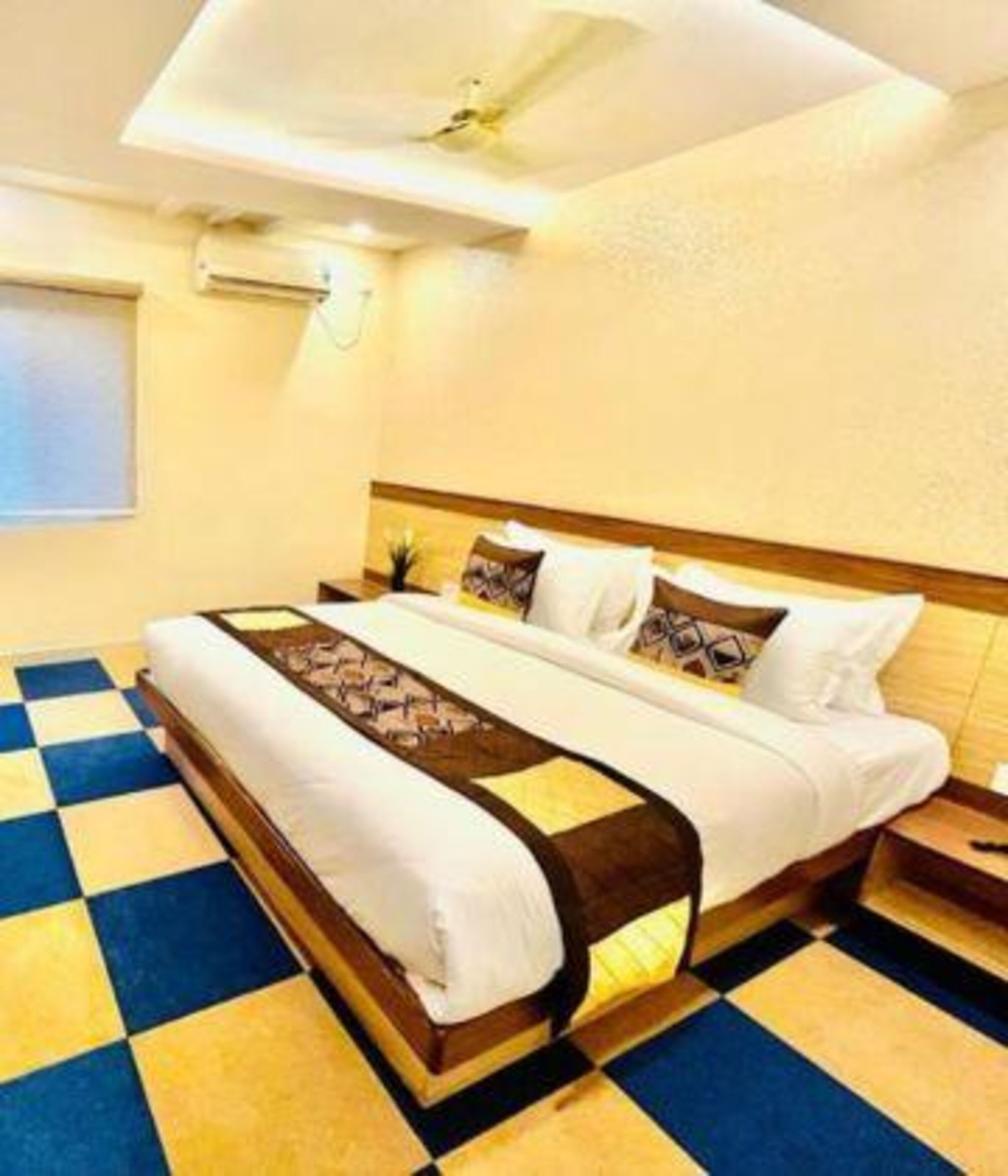 Una habitación de hotel con piso a cuadros, una cama con cubrecama blanco y marrón, y un cabecero de madera.