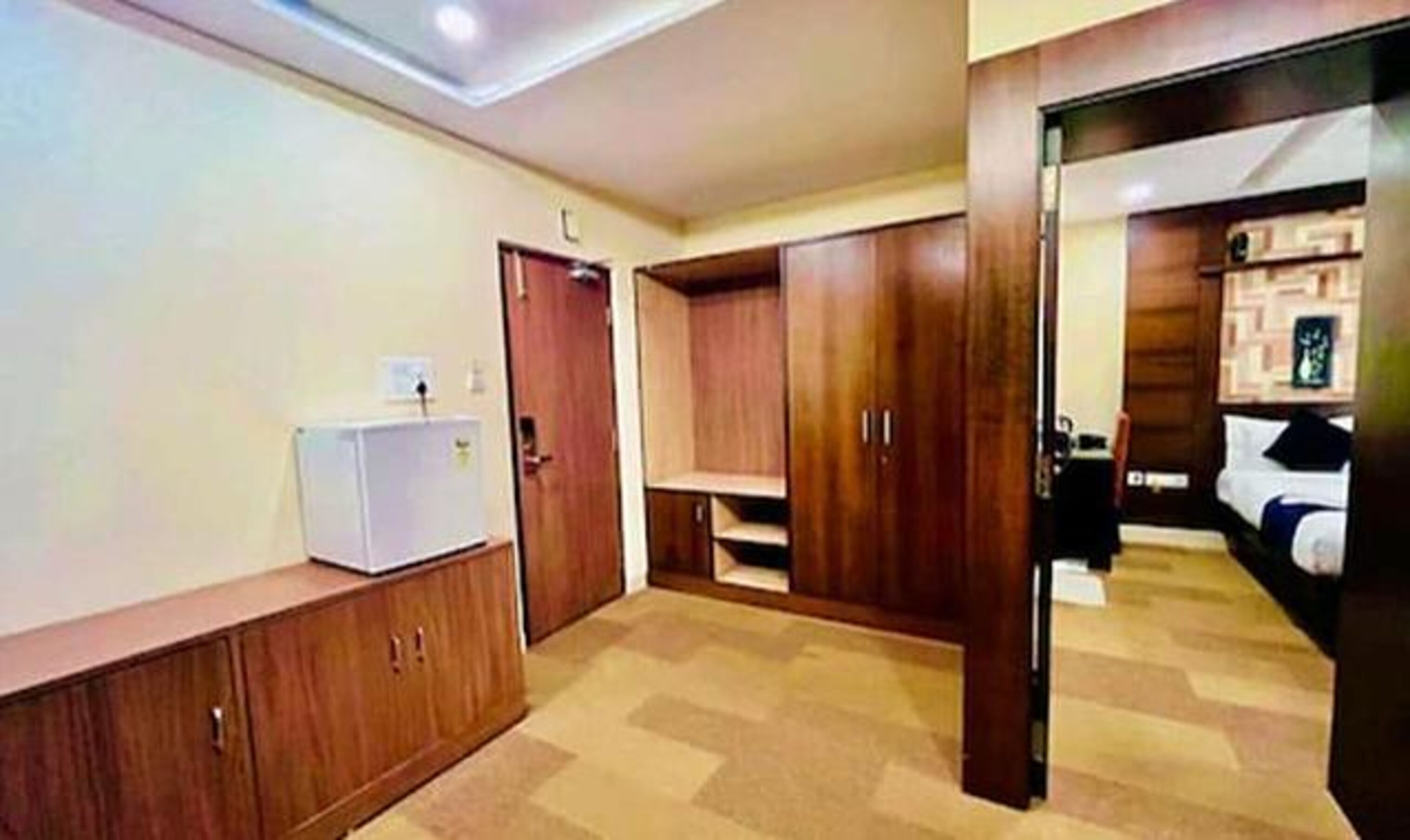 A room with wooden wardrobes, a white refrigerator, and a bed with a black and white duvet.