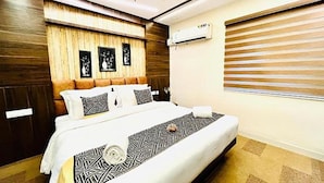 Ein Schlafzimmer mit hölzernem Kopfteil, einem Bett mit gemusterten Bettbezügen, einer Klimaanlage und einem Fenster mit Jalousien.