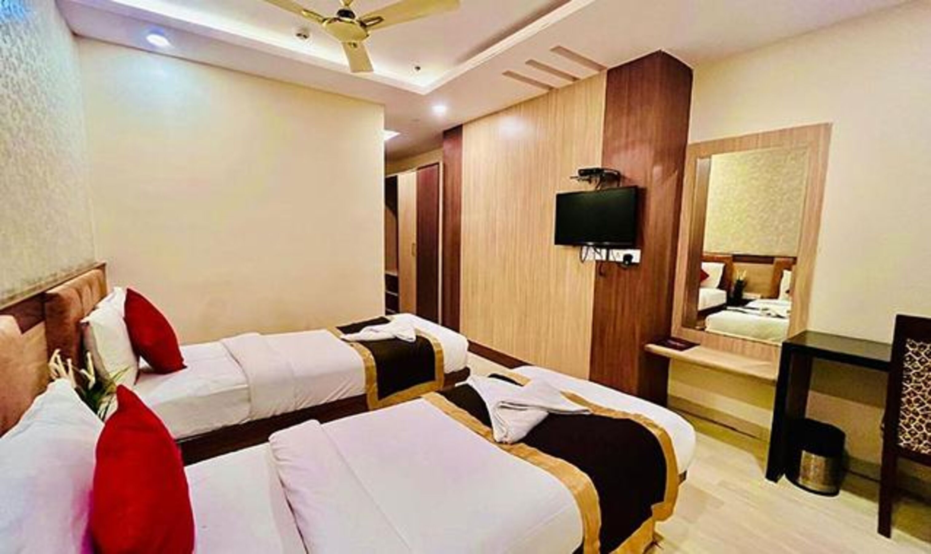 A hotel room with two beds, a television, a mirror, and a small table.