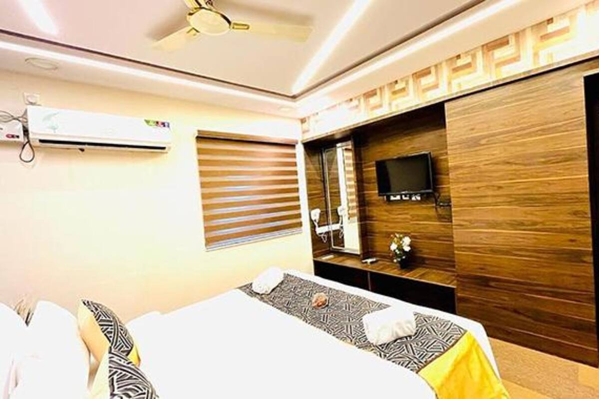 Ein Hotelzimmer mit Bett, Fernseher, Holzschrank und einem Fenster mit Jalousien.