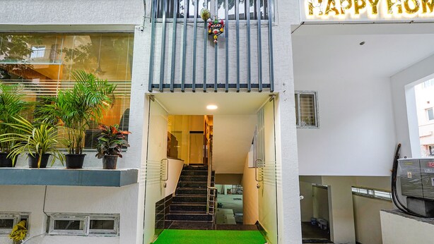 A hotel entrance with a green mat, a staircase leading to the interior, and a balcony with potted plants. - FabHotel Happy Home Stay (Bengaluru)