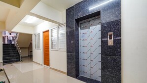 A hallway with a polished floor, a wooden door, and a marble elevator with a digital display. - FabHotel Happy Home Stay (Bengaluru)