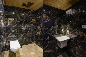 A modern bathroom with black marble walls, a white toilet, a bathtub, and a glass shower enclosure. - Fabhotel Antlers (Mumbai)