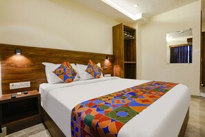 A modern hotel room with a large bed, wooden headboard, and a colorful geometric-patterned bedspread. - Fabhotel Antlers (Mumbai)