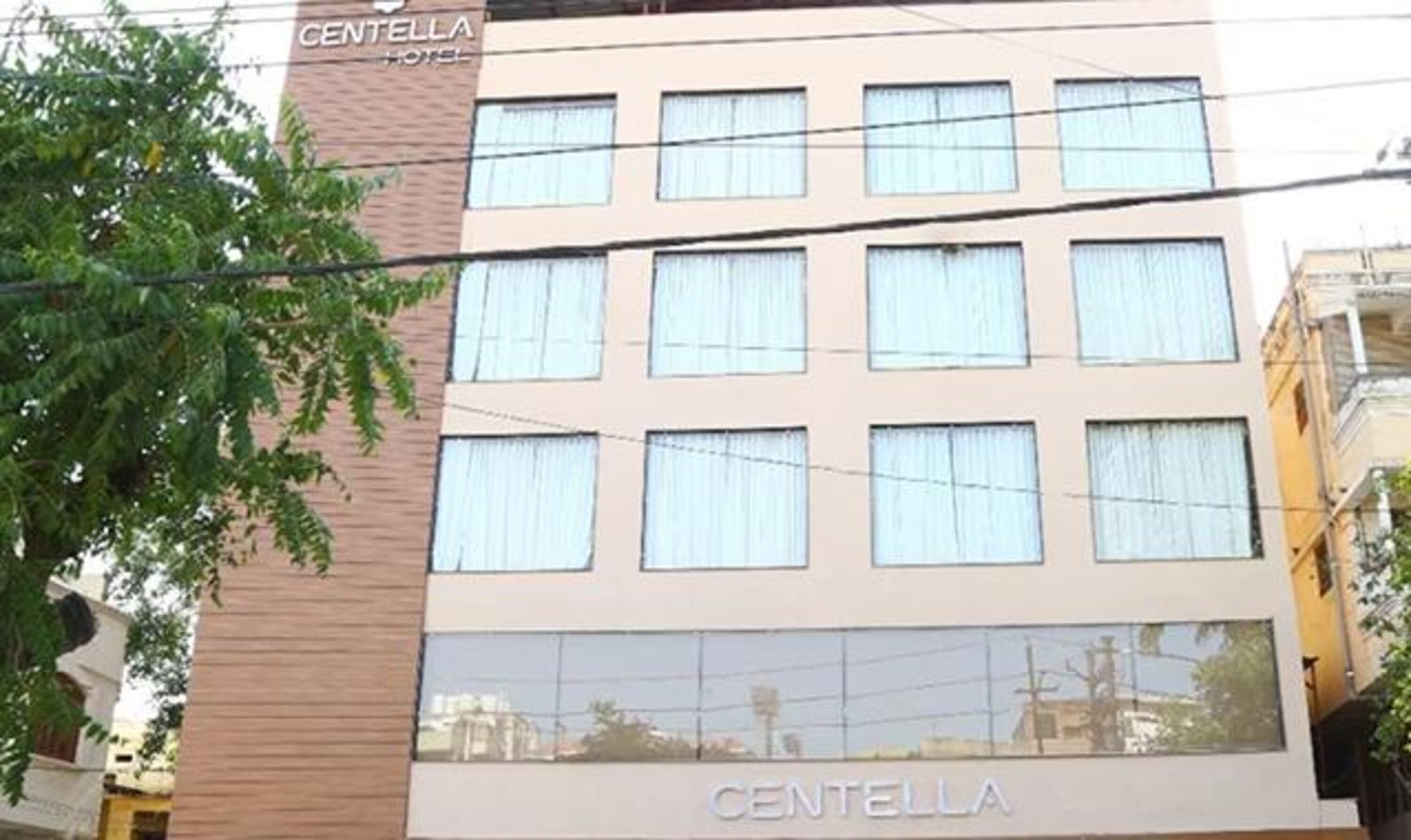A multi-story hotel named Centella with a modern facade, multiple windows, and a visible reflection of the surrounding area.