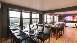 A dining area with tables and chairs, large windows, and a bar area with bottles. - Fabhotel Grover (Kangra)
